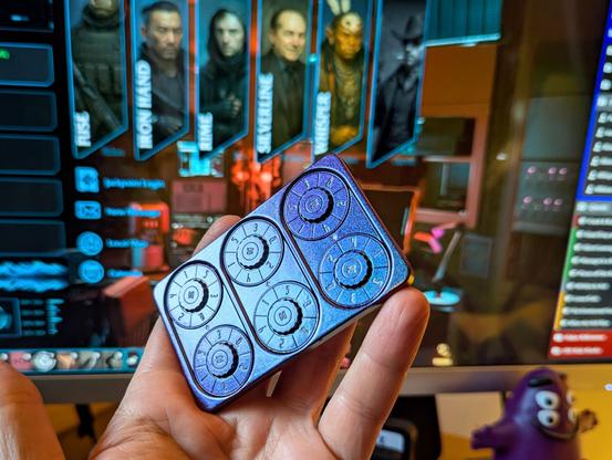 A thick metal card in sparkly purple or green, depending on the angle, with 6 dials, each representing a D6 with tiny white text. It’s in my hand held up in front of a computer screen showing cyberpunk character art, diagnostics, and game notes.