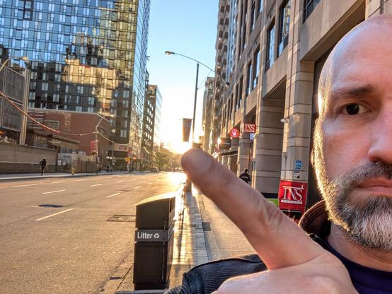 Selfie of me pointing at the sun as it's setting almost down the center of Toronto city Street.
