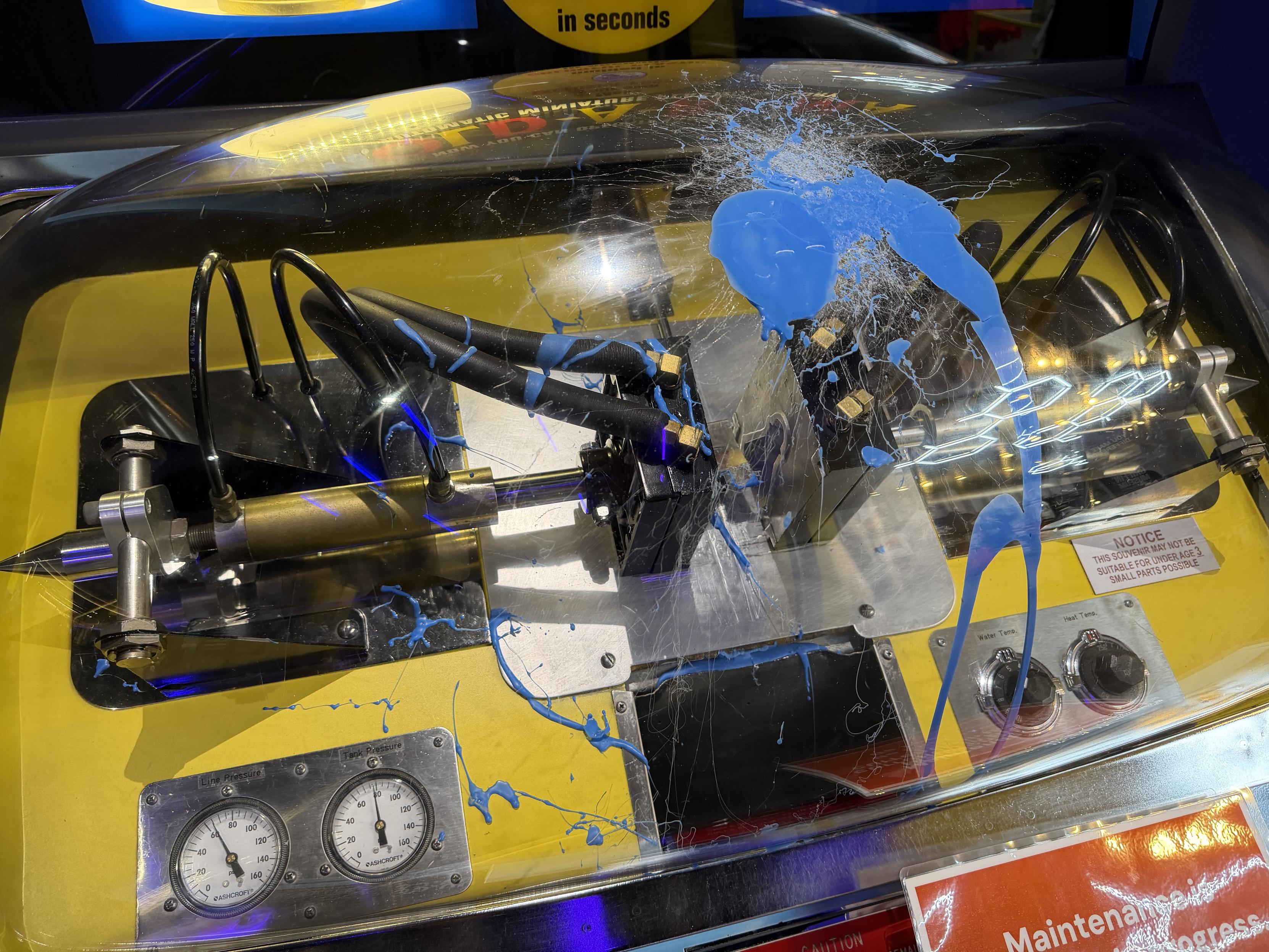 A closer view of a Mold-O-Rama machine with a maintenance sign. A previous mold must have burst because there’s dried blue wax on the inside of the clear dome. This angle is off to the left side and closer to the burst wax