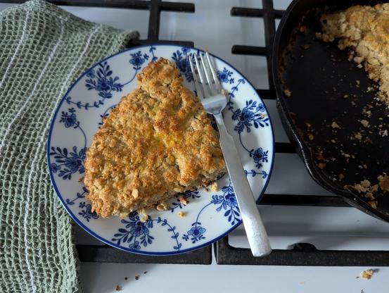 One golden wedge of chunky oats, oat flour, and bits of rosemary sitting on a white and blue plate.