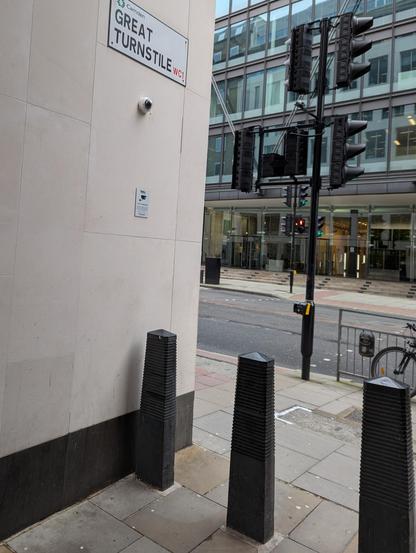 A street sign reading “Great turnstile” mounted on a wall above three bollards that are leading into a narrow alley.