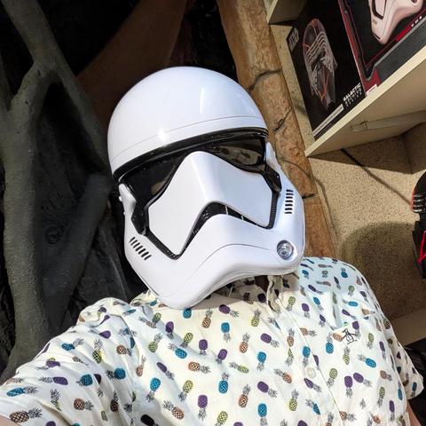 Selfie in a white storm trooper helmet and a white short sleeved collared shirt covered in multicolored pineapples.