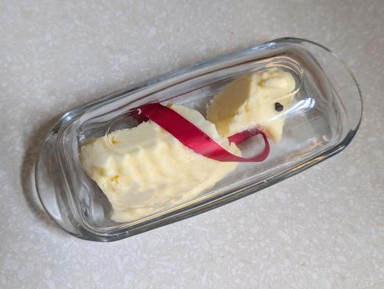 A butter lamb in a glass butter dish with the lamb’s head chopped off and placed next to the body so it fits under the glass lid.