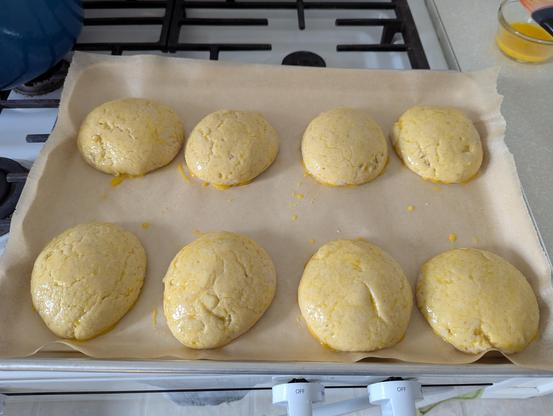 Eight flattened four inch balls of dough, freshly egg washed, on a half sheet lined with parchment.