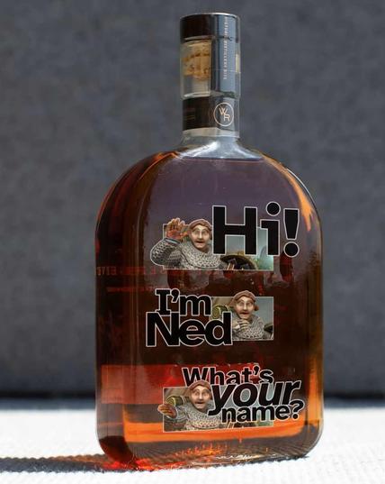 A glass bottle of brownish liquor, and printed on the glass are three images of a doughy guy with a mop of red hair and moustache, wearing chain mail, waving and saying “Hi!” In the second image he has his hand on his chest and says, “I’m Ned.” In the third, he’s gesturing to the viewer and asking, “What’s your name?”