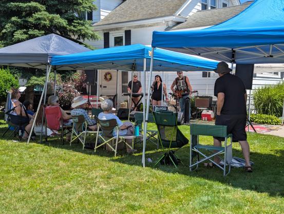 Assorted lawn chairs across a double-wide lawn with five person band — keyboard, guitar, bass, drums, vocalist.