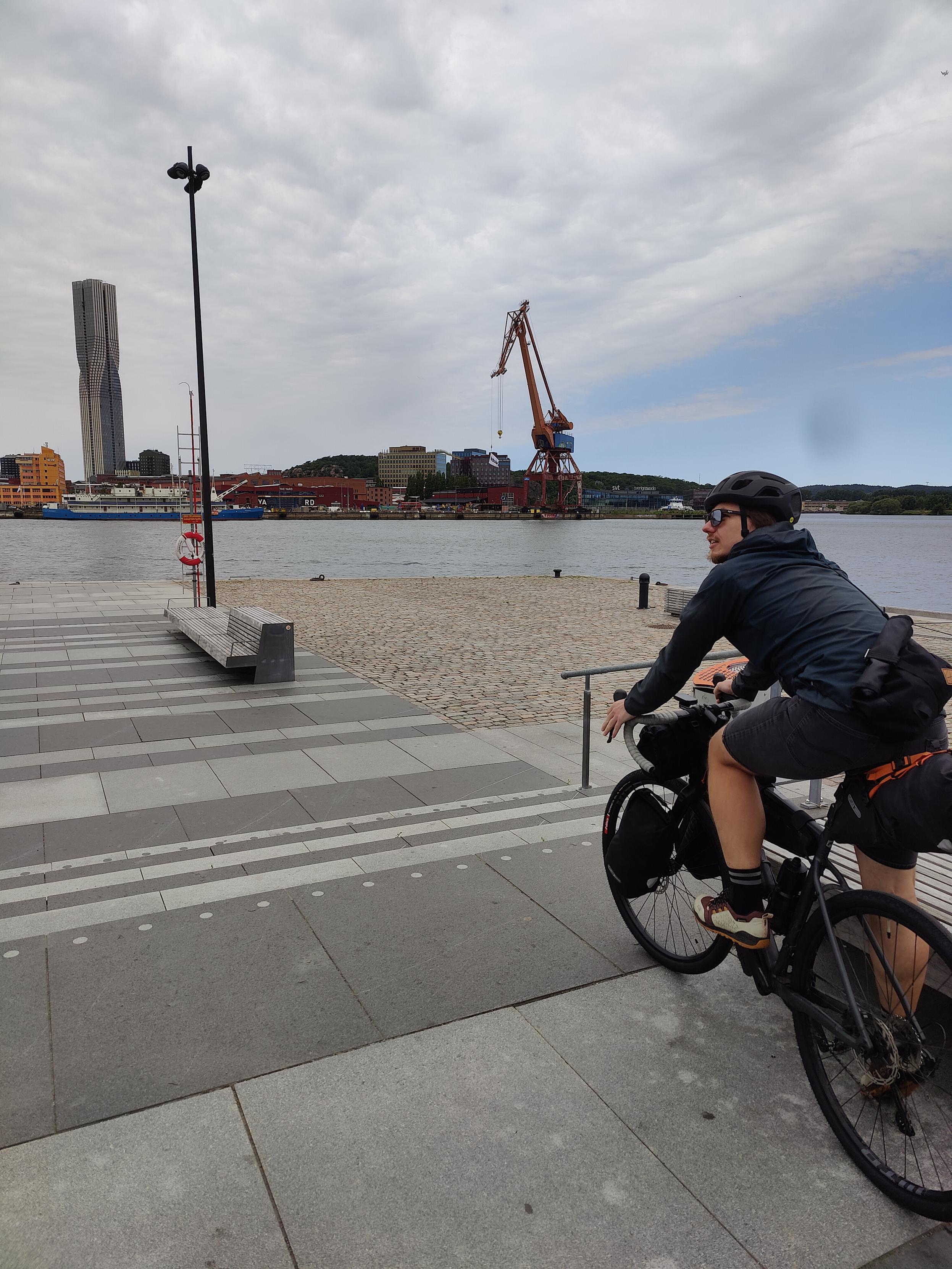 Cyclist in Gotheborg next to the water, crane and tower visible on the other side.