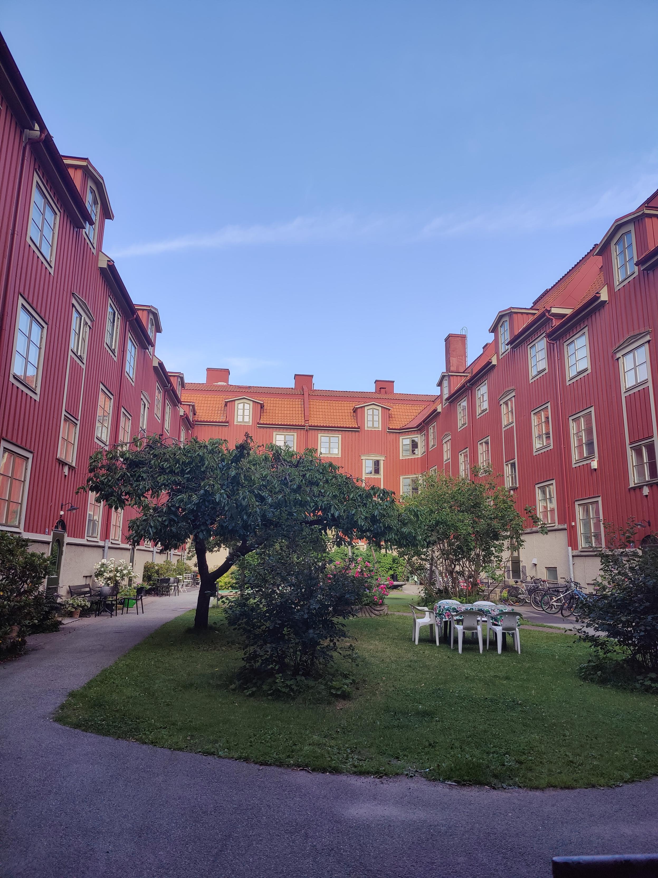 A green courtyard, all the surrounding buildings are painted red.