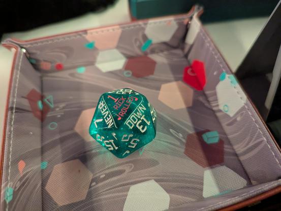 A large glitter-filled transparent teal 20-sided die sitting with the number 1 showing in pink with the text “Rick Roll”; the three adjacent faces are “7 never”, “19 let”, and “13 down”.