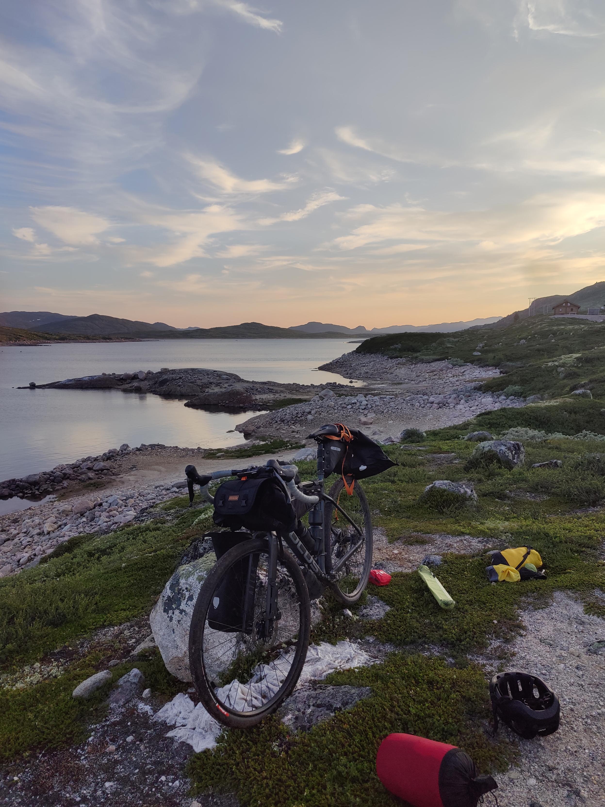 Gravel bicycle next to a lake, tent equipment on the ground.