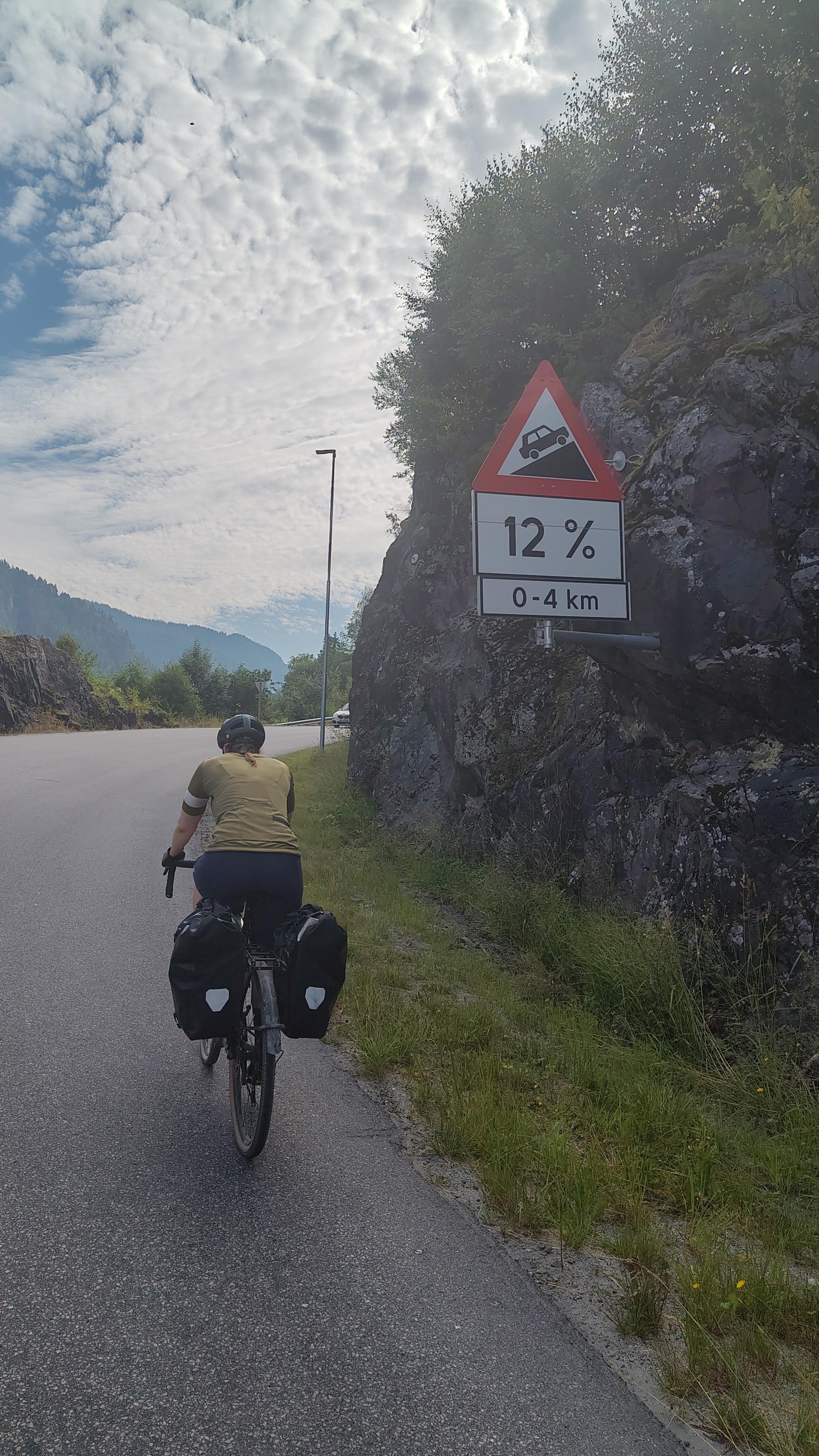 Cyclist on a climb, sign saying the grade is 12%.