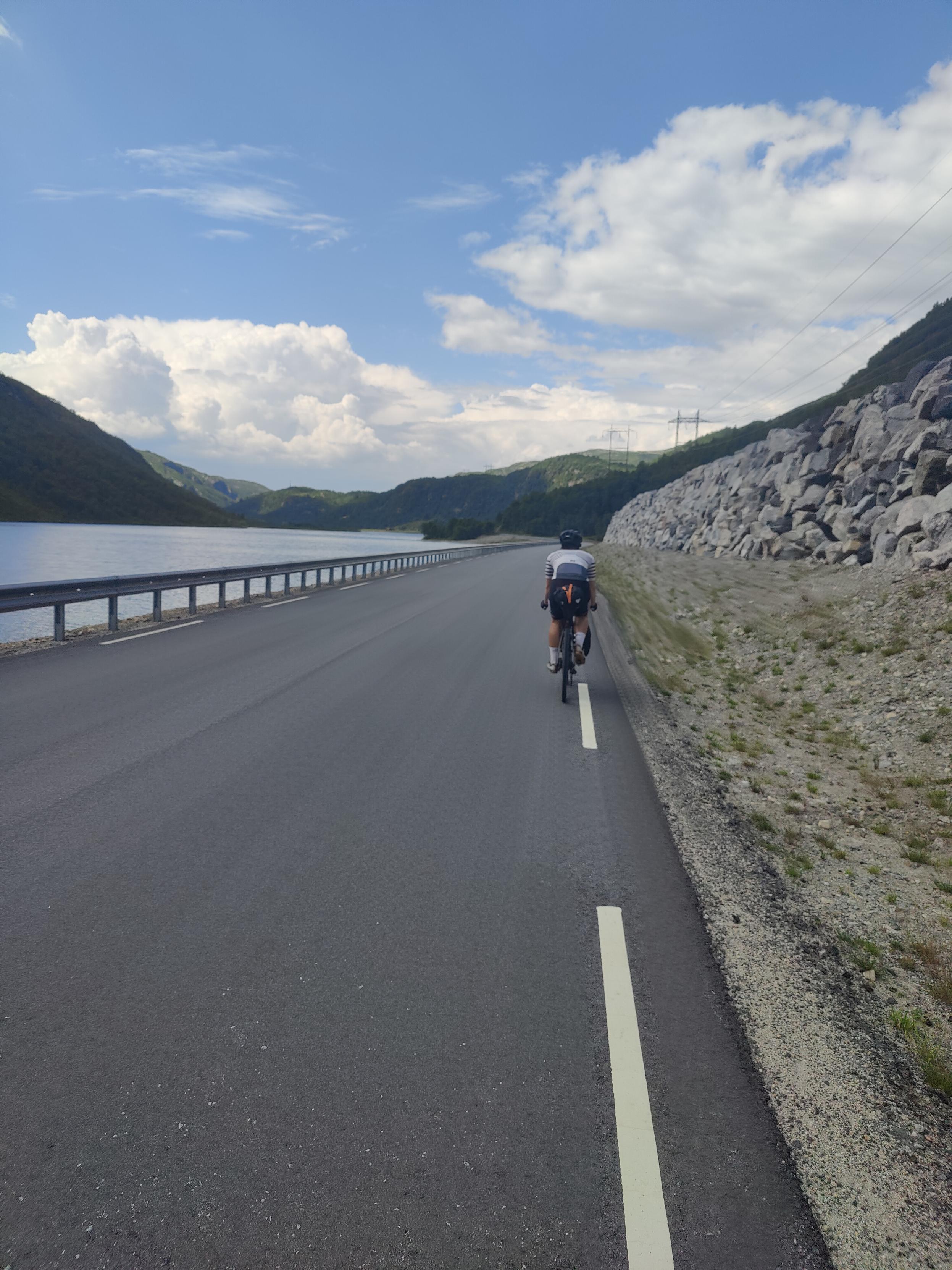 Cyclist on the road, lake on the left side.