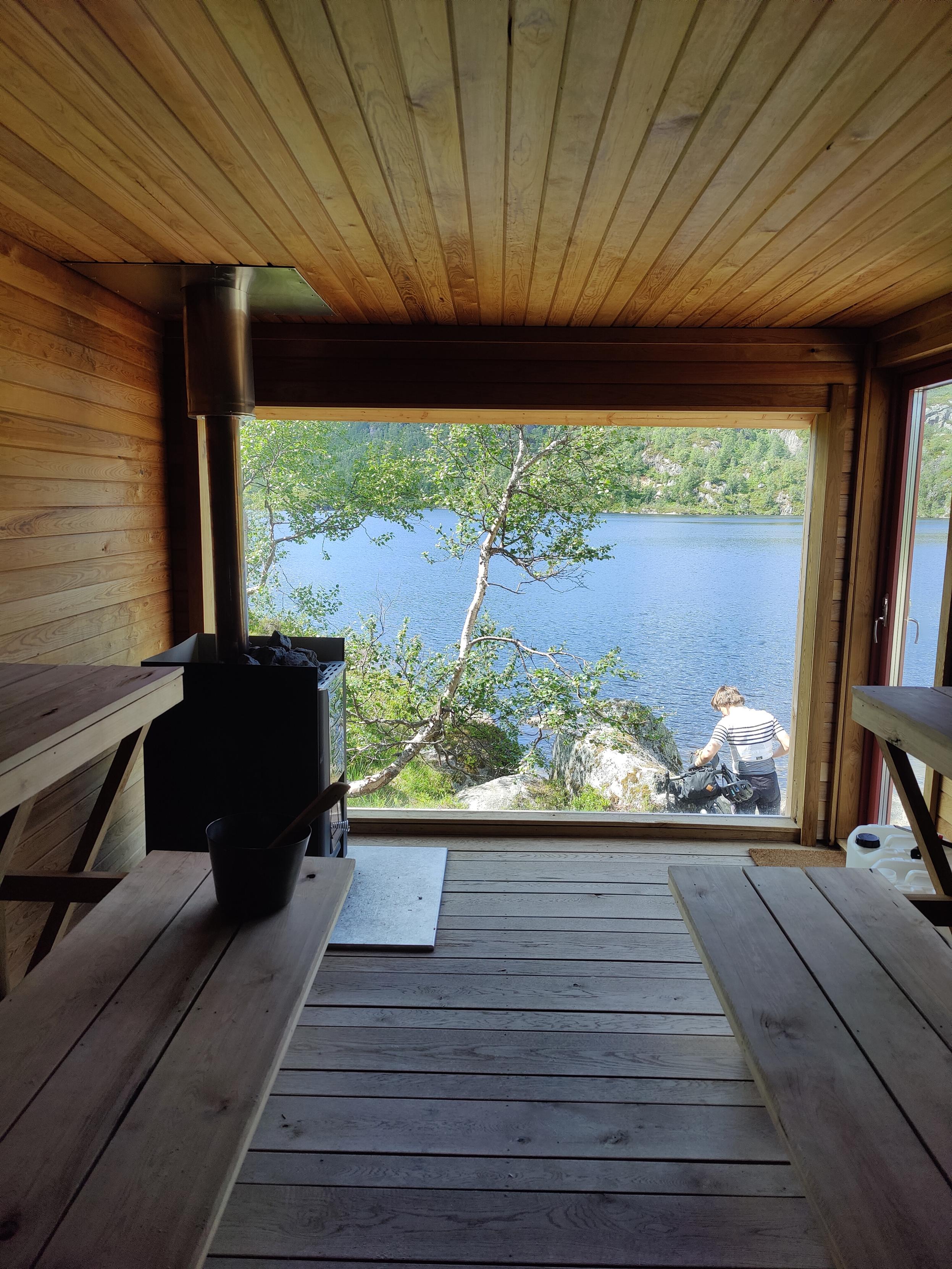 View from a sauna, lake and cyclist visible outside.