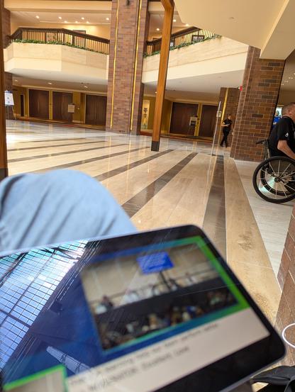 The closed room visible across a vast hotel atrium, looking over a tablet balanced on my leg with a video feed of the talk, including captions and an ASL interpreter.