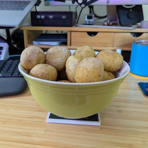 A porcelain serving bowl filled with at least four pounds of salt potatoes sitting next to a keyboard on a computer desk.