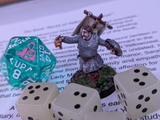 A gaming mini of a slightly doughy white human with brown hair and mustache in chainmail holding a holy symbol up at arms’ length, surrounded by some six-sided dice with uneven dots and a large D20 with an image of Rick Astley in the 20 position.